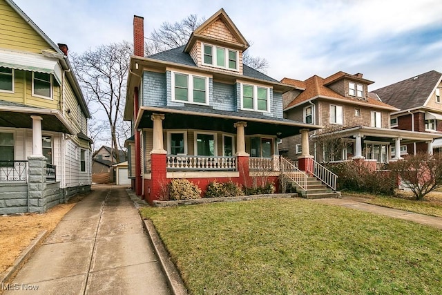 american foursquare style home featuring an outbuilding, covered porch, a chimney, and a front yard