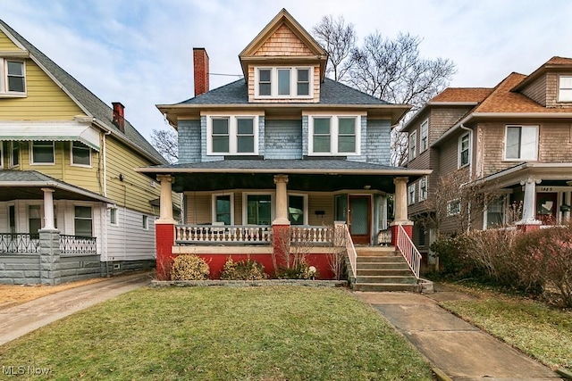 traditional style home with covered porch, roof with shingles, and a front yard