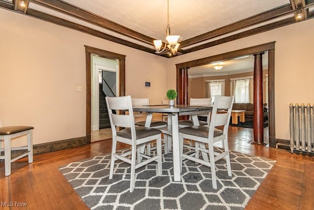 dining area featuring decorative columns, radiator, wood-type flooring, crown molding, and a chandelier