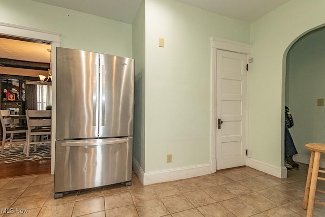 kitchen featuring arched walkways, light tile patterned floors, freestanding refrigerator, and baseboards