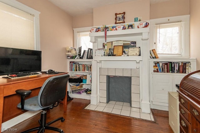 home office with a tile fireplace, wood finished floors, and a healthy amount of sunlight