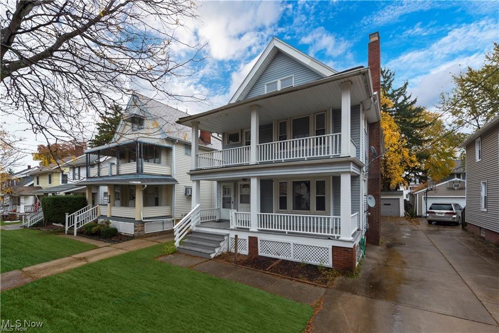 view of front facade featuring a balcony, covered porch, an outdoor structure, a front lawn, and a chimney