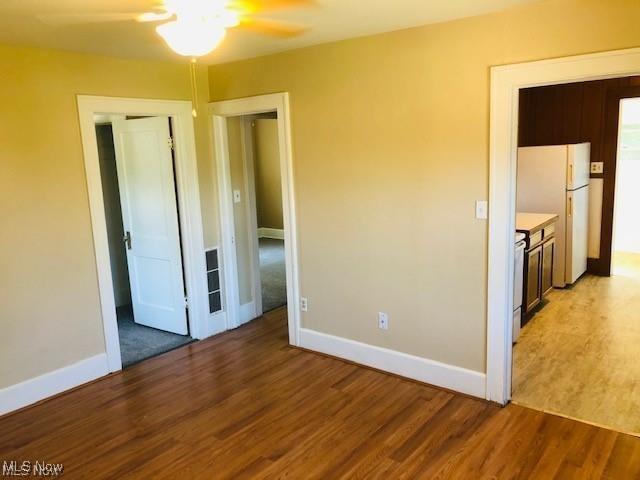 unfurnished bedroom with a ceiling fan, freestanding refrigerator, baseboards, and light wood finished floors