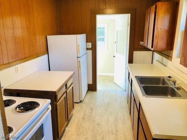 kitchen with white appliances, light wood-style flooring, light countertops, wood walls, and a sink