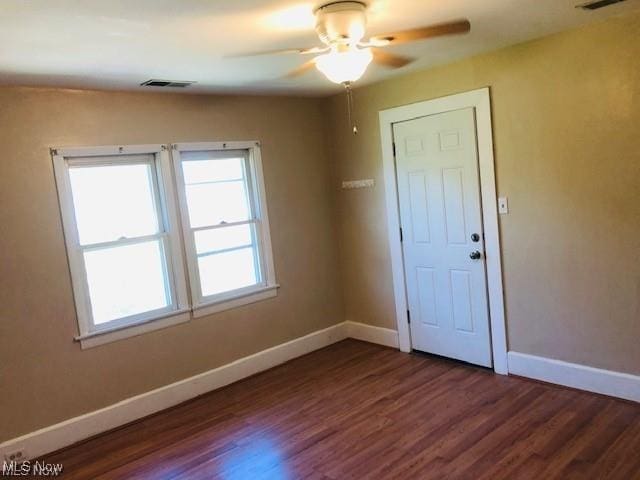 spare room featuring a ceiling fan, dark wood finished floors, visible vents, and baseboards