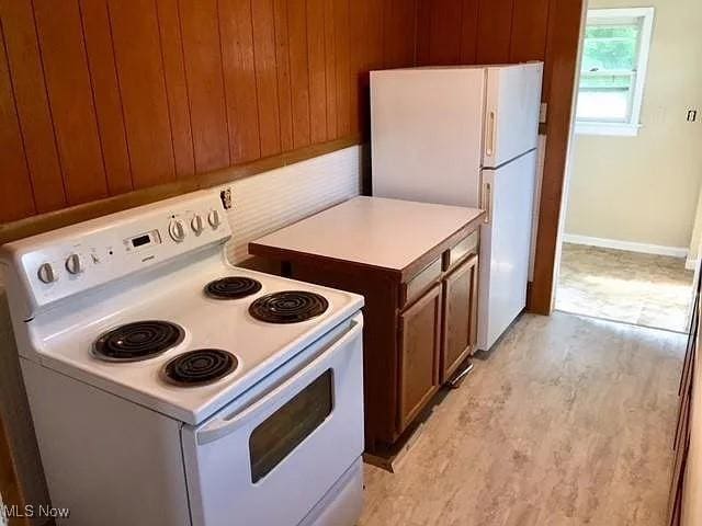 kitchen with brown cabinets, white appliances, wooden walls, and light countertops