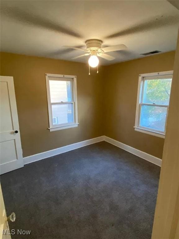 empty room featuring a ceiling fan, dark colored carpet, visible vents, and baseboards