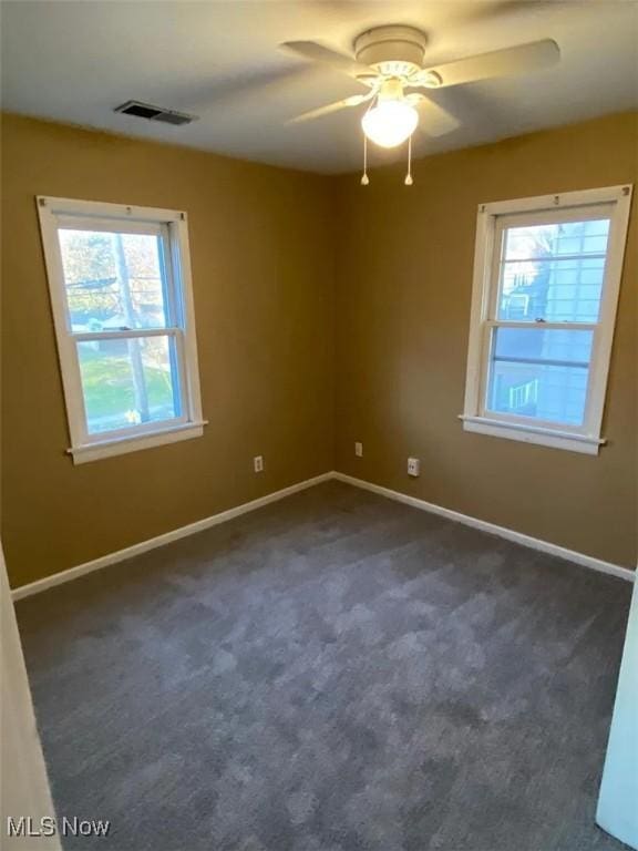 spare room with dark colored carpet, a ceiling fan, visible vents, and baseboards