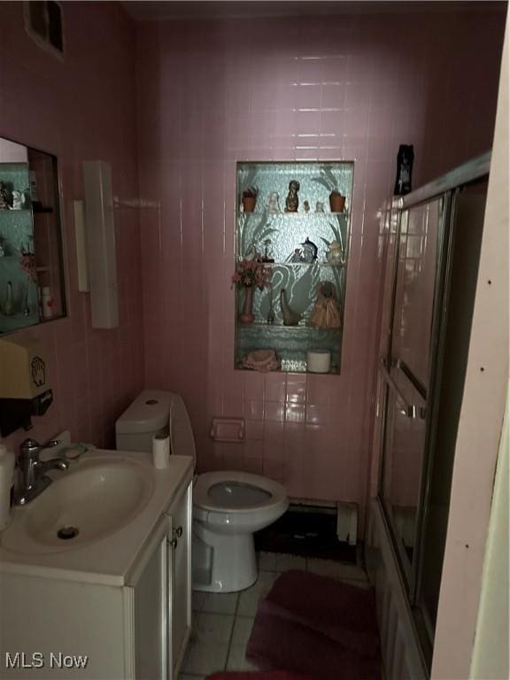 full bathroom with tile walls, toilet, a shower with shower door, vanity, and tile patterned flooring