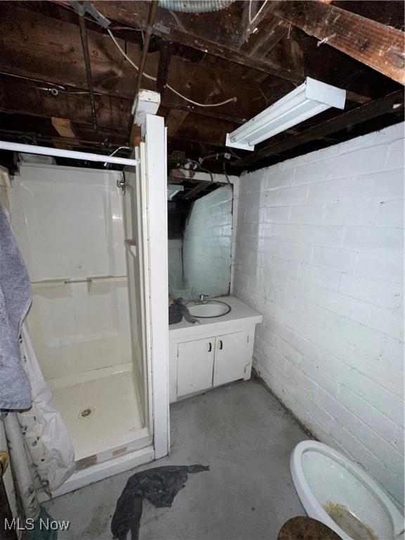 bathroom featuring concrete flooring, toilet, vanity, a shower stall, and concrete block wall