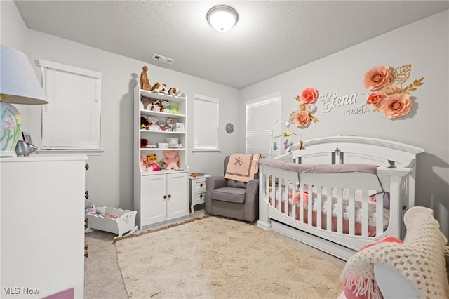 carpeted bedroom with a nursery area, visible vents, and a textured ceiling