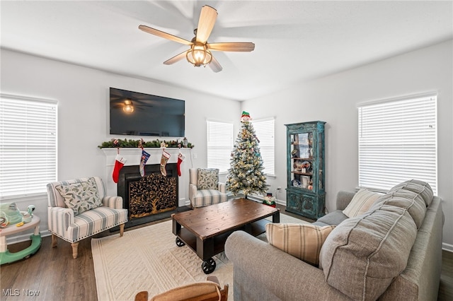 living area featuring ceiling fan, a fireplace, baseboards, and wood finished floors