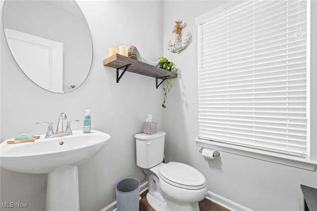 half bath with baseboards, a sink, and toilet