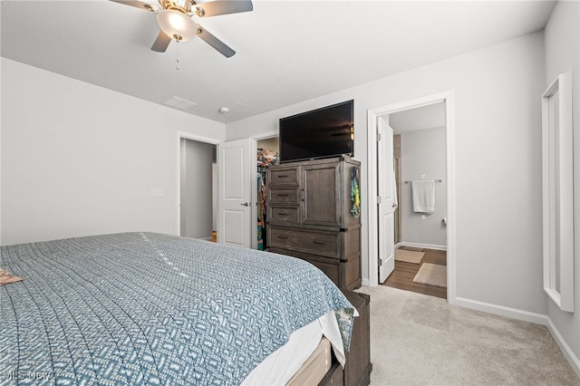 carpeted bedroom with a ceiling fan, a walk in closet, ensuite bath, and baseboards