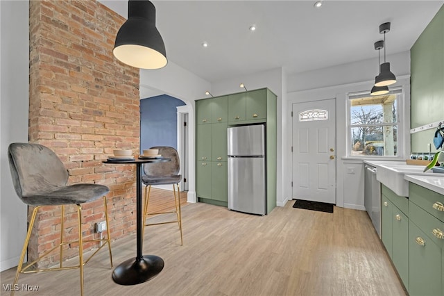 kitchen with light wood finished floors, appliances with stainless steel finishes, arched walkways, and green cabinetry