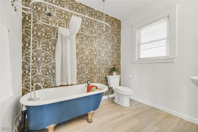 bathroom featuring toilet, baseboards, a freestanding bath, and wood finished floors