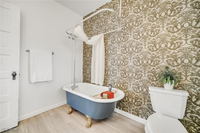 bathroom featuring toilet, a soaking tub, baseboards, and wood finished floors