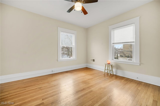 spare room featuring hardwood / wood-style flooring, visible vents, baseboards, and a wealth of natural light