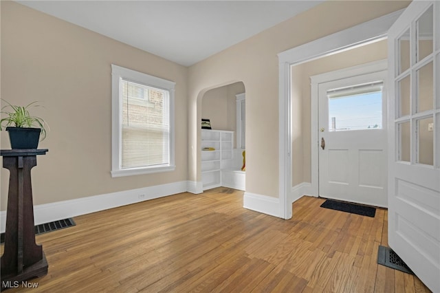 entrance foyer with light wood-type flooring, a wealth of natural light, arched walkways, and baseboards