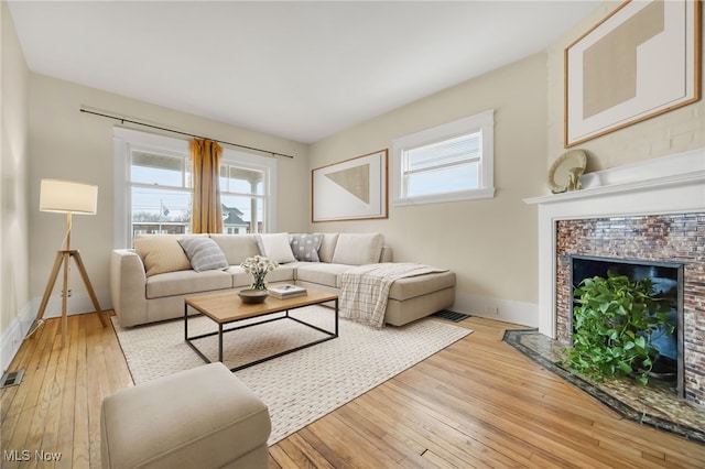 living area featuring light wood-type flooring, a healthy amount of sunlight, a fireplace with flush hearth, and visible vents