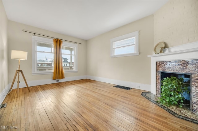 unfurnished living room with a healthy amount of sunlight, a fireplace with flush hearth, visible vents, and hardwood / wood-style floors