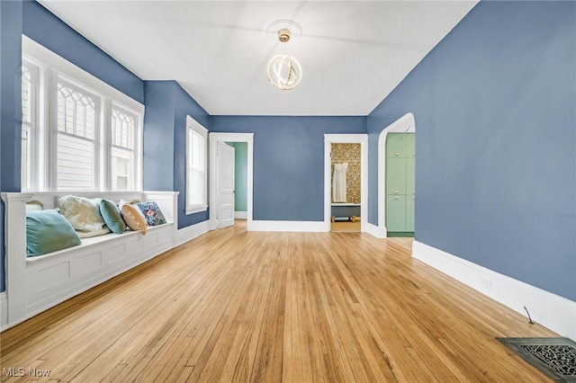 interior space with light wood-style floors, baseboards, visible vents, and arched walkways