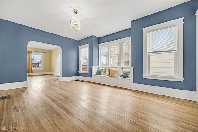 spare room featuring arched walkways, wood-type flooring, and baseboards