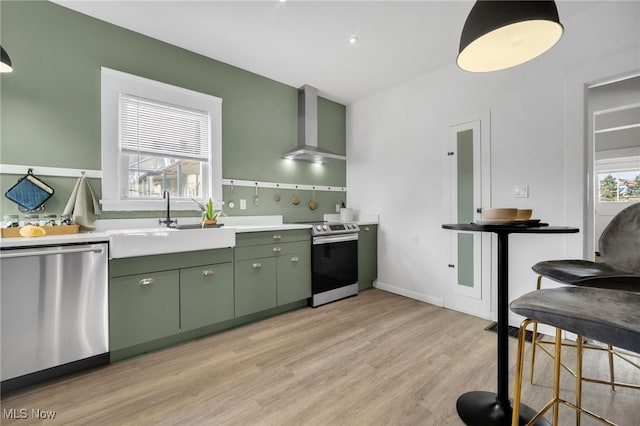 kitchen featuring light wood-style flooring, a sink, appliances with stainless steel finishes, wall chimney exhaust hood, and green cabinetry