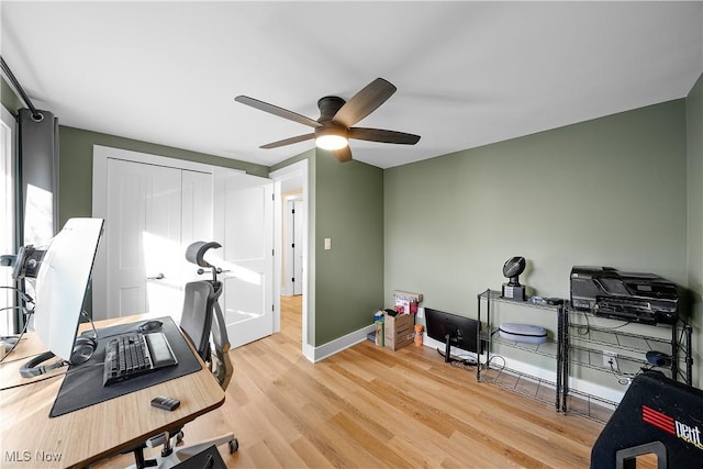 exercise area with light wood-type flooring, ceiling fan, and baseboards