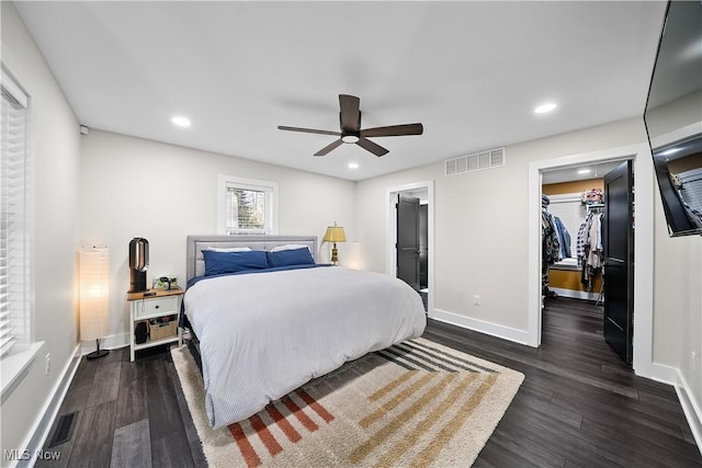 bedroom with baseboards, visible vents, dark wood finished floors, a walk in closet, and recessed lighting