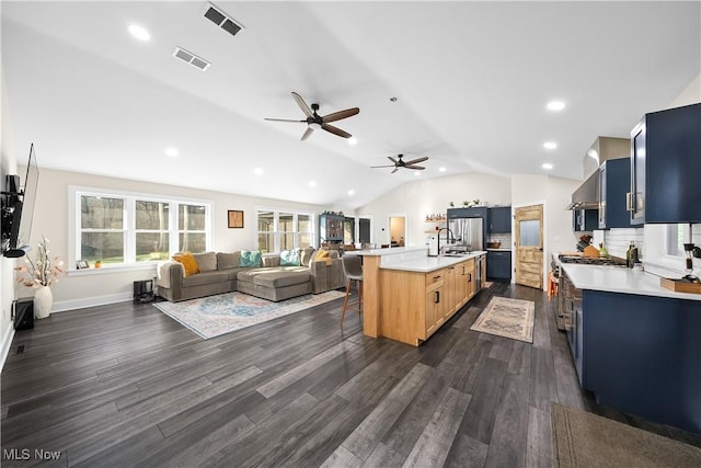 kitchen with visible vents, open floor plan, blue cabinets, a kitchen bar, and a sink