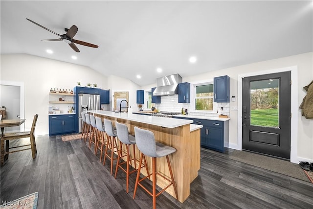 kitchen featuring blue cabinetry, wall chimney exhaust hood, appliances with stainless steel finishes, and light countertops