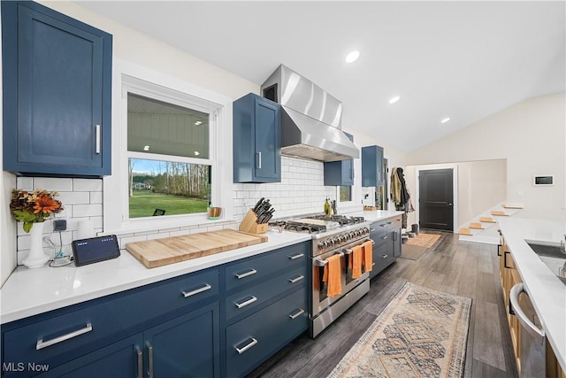 kitchen with appliances with stainless steel finishes, dark wood-type flooring, vaulted ceiling, blue cabinets, and wall chimney exhaust hood