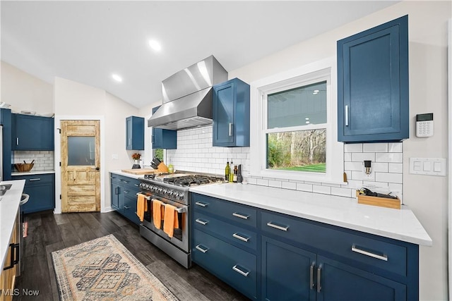 kitchen featuring dark wood finished floors, lofted ceiling, light countertops, stainless steel stove, and wall chimney range hood