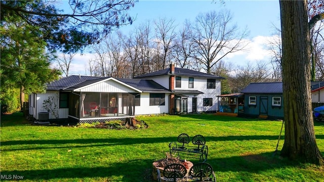 back of property with metal roof, cooling unit, a sunroom, a yard, and a chimney