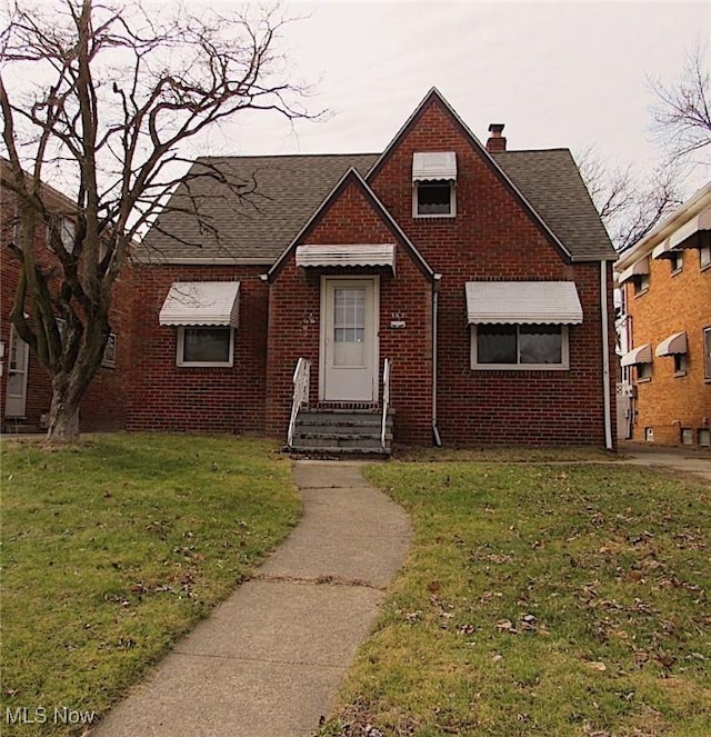 view of front of property with brick siding, a chimney, a shingled roof, a front yard, and entry steps