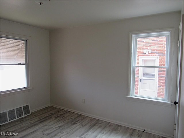 unfurnished room with wood finished floors, visible vents, and baseboards