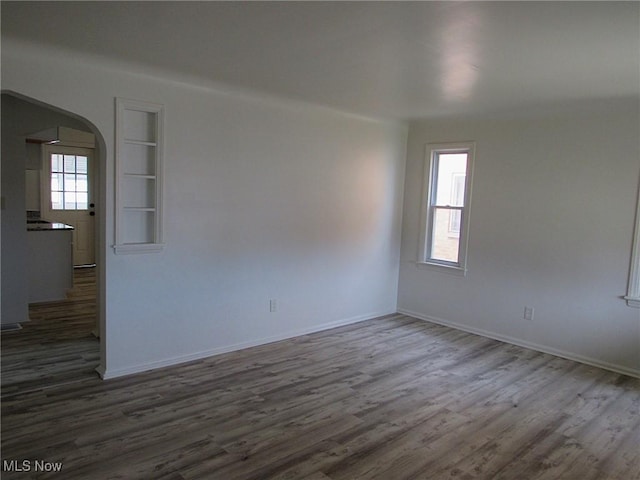 unfurnished room featuring baseboards, built in shelves, arched walkways, and wood finished floors