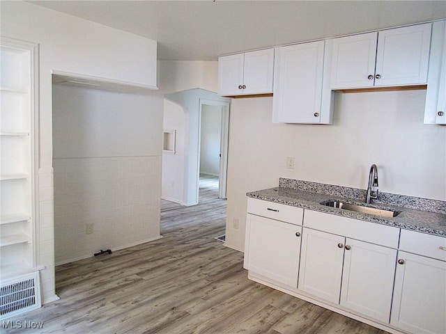 kitchen featuring visible vents, light wood-style flooring, stone countertops, white cabinetry, and a sink