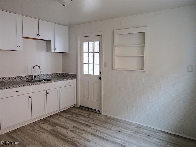 kitchen with stone countertops, white cabinets, light wood-style flooring, a sink, and tile walls