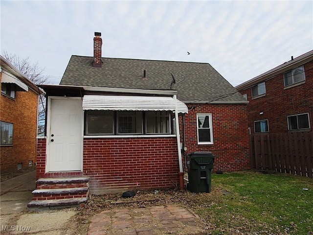 rear view of property with brick siding, fence, a chimney, and roof with shingles