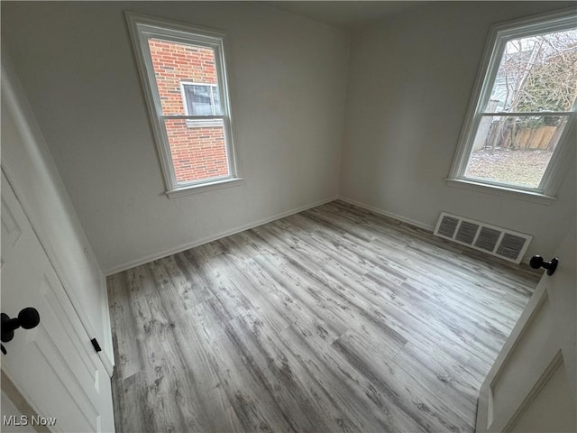 empty room featuring wood finished floors, visible vents, and baseboards