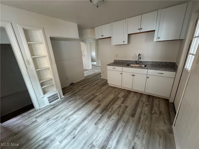 kitchen featuring visible vents, white cabinets, dark countertops, wood finished floors, and a sink