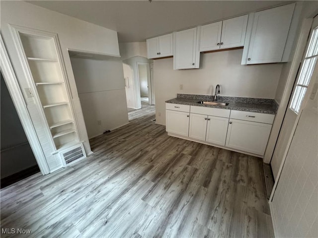 kitchen featuring visible vents, white cabinets, a sink, and wood finished floors