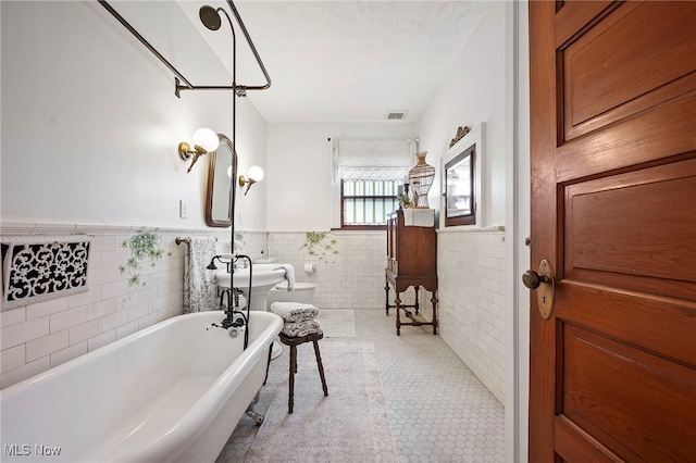 bathroom featuring visible vents, a wainscoted wall, tile patterned flooring, a freestanding bath, and tile walls