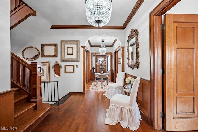 foyer entrance featuring arched walkways, an inviting chandelier, ornamental molding, wainscoting, and hardwood / wood-style flooring