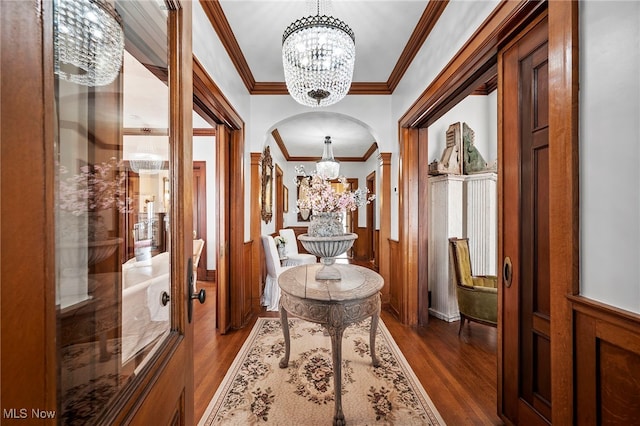 hall featuring ornamental molding, arched walkways, dark wood finished floors, and a notable chandelier