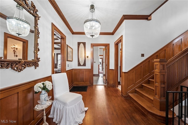 foyer entrance featuring a notable chandelier, dark wood-type flooring, stairs, wainscoting, and crown molding