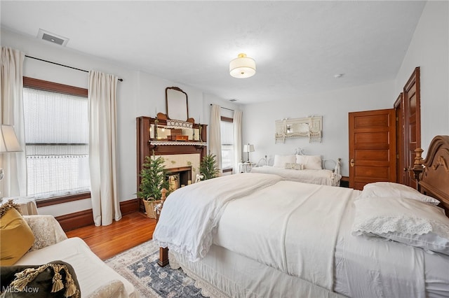 bedroom with multiple windows, a fireplace, wood finished floors, and visible vents