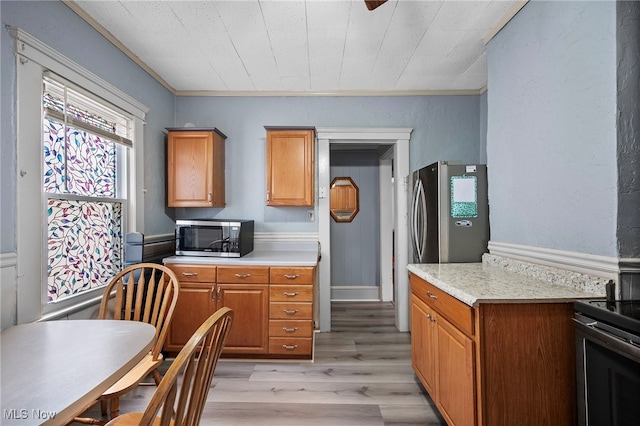 kitchen with stainless steel appliances, brown cabinetry, light countertops, and light wood finished floors